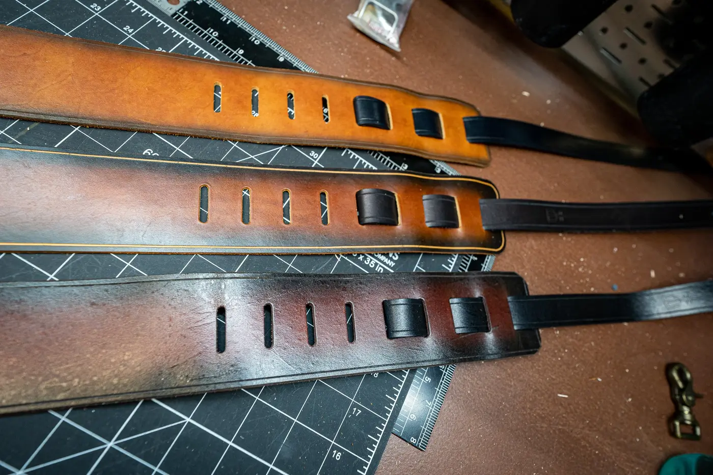 Three finished leather guitar straps with airbrushed edges on the workbench